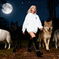 Woman in a white hoodie standing among wolves under a moonlit sky