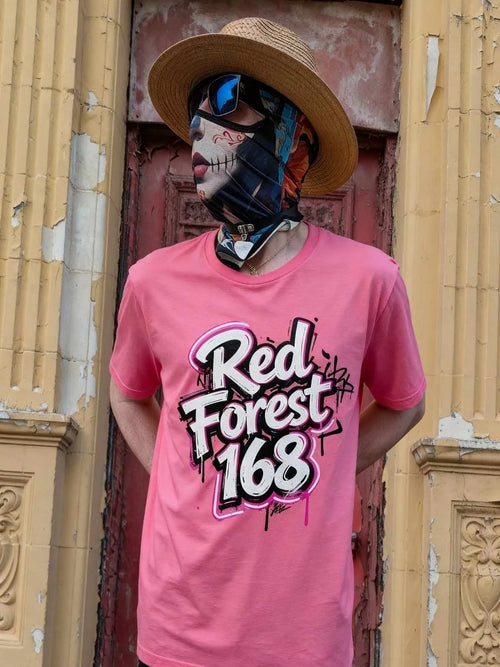 Person wearing a pink 'Red Forest 168' t-shirt with a colorful mask and hat in front of a textured wall.