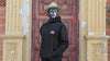 The Sun Walker, wearing an Albert Harry AH minimal White Knight black hoodie, sunglasses, and a Summer straw hat, walking down the street at the Trafford Park Hotel.